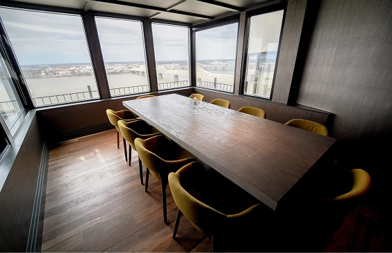 Modern conference room with a large wooden table, yellow chairs, and panoramic windows overlooking a river and cityscape. Swizzle calls this “Al’s Table”.